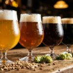 Quatro taças de cerveja artesanal dourada, âmbar, marrom e preta no balcão de um pub