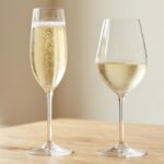 Taça flûte de espumante ao lado de taça de vinho frisante sobre mesa de madeira clara