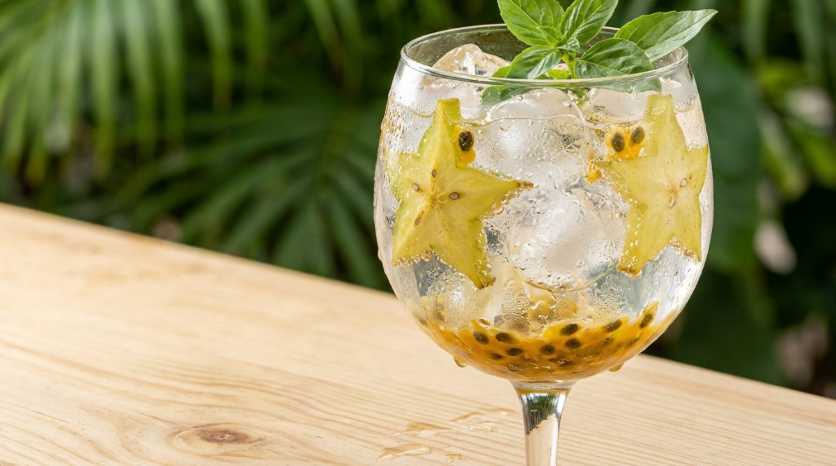Taça de gin tônica com carambola, maracujá e manjericão